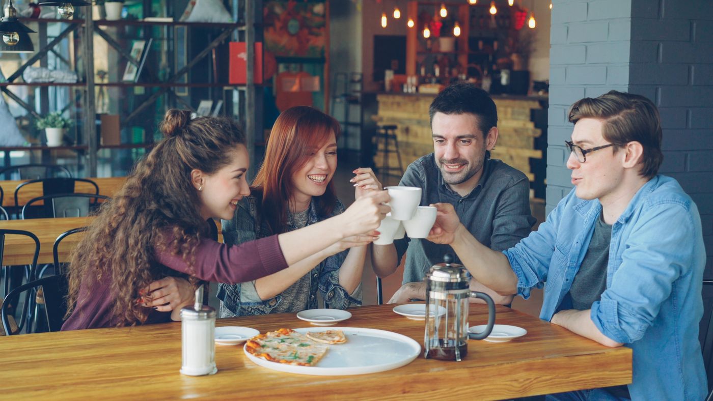 Four friends raising their coffee mugs together in a toast at a café